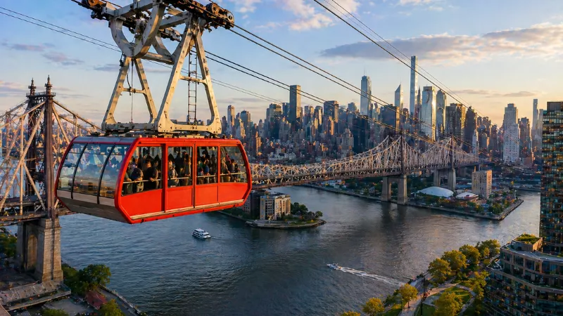 Roosevelt Island Tramway over East River with New York City skyline and bridge views in daytime
