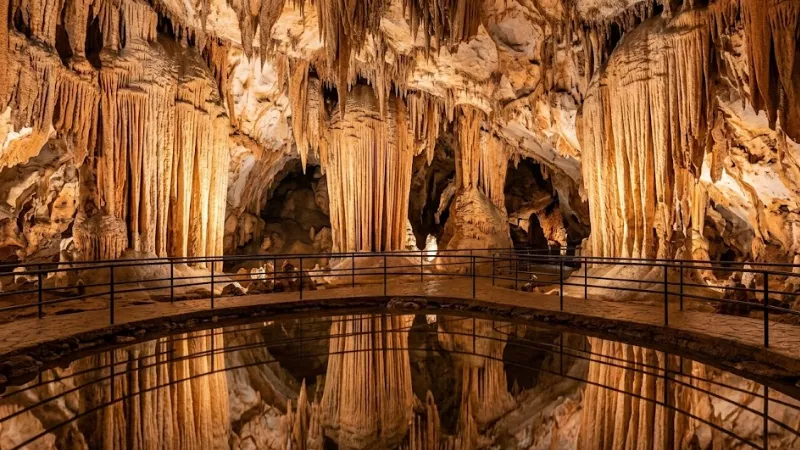 Wide interior view of Luray Caverns Virginia with warm-lit stalactite formations reflected in a still underground pool