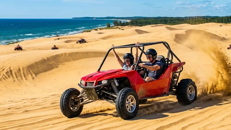 Red dune buggy kicking up sand with excited riders on Silver Lake Sand Dunes Michigan with Lake Michigan in background