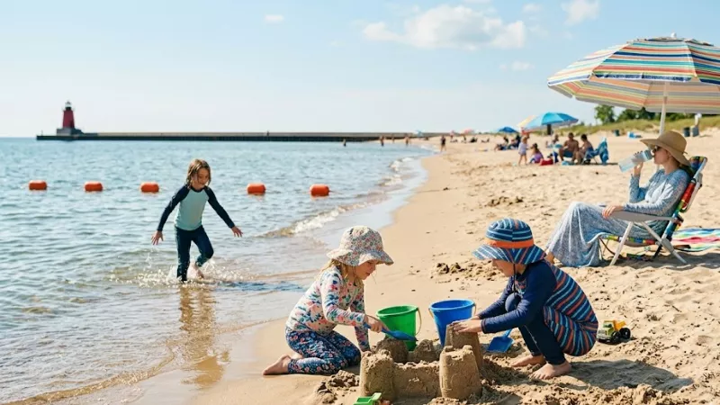 Children building a sandcastle and wading in the buoyed swim area at Charles Mears State Park beach in Pentwater