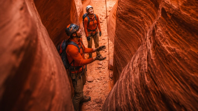 group of hikers rappelling through a narrow red sandstone slot canyon while canyoneering near Kanab Utah