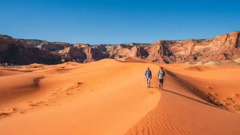 Two hikers walking up coral-colored sand dunes at Coral Pink Sand Dunes State Park near Kanab Utah
